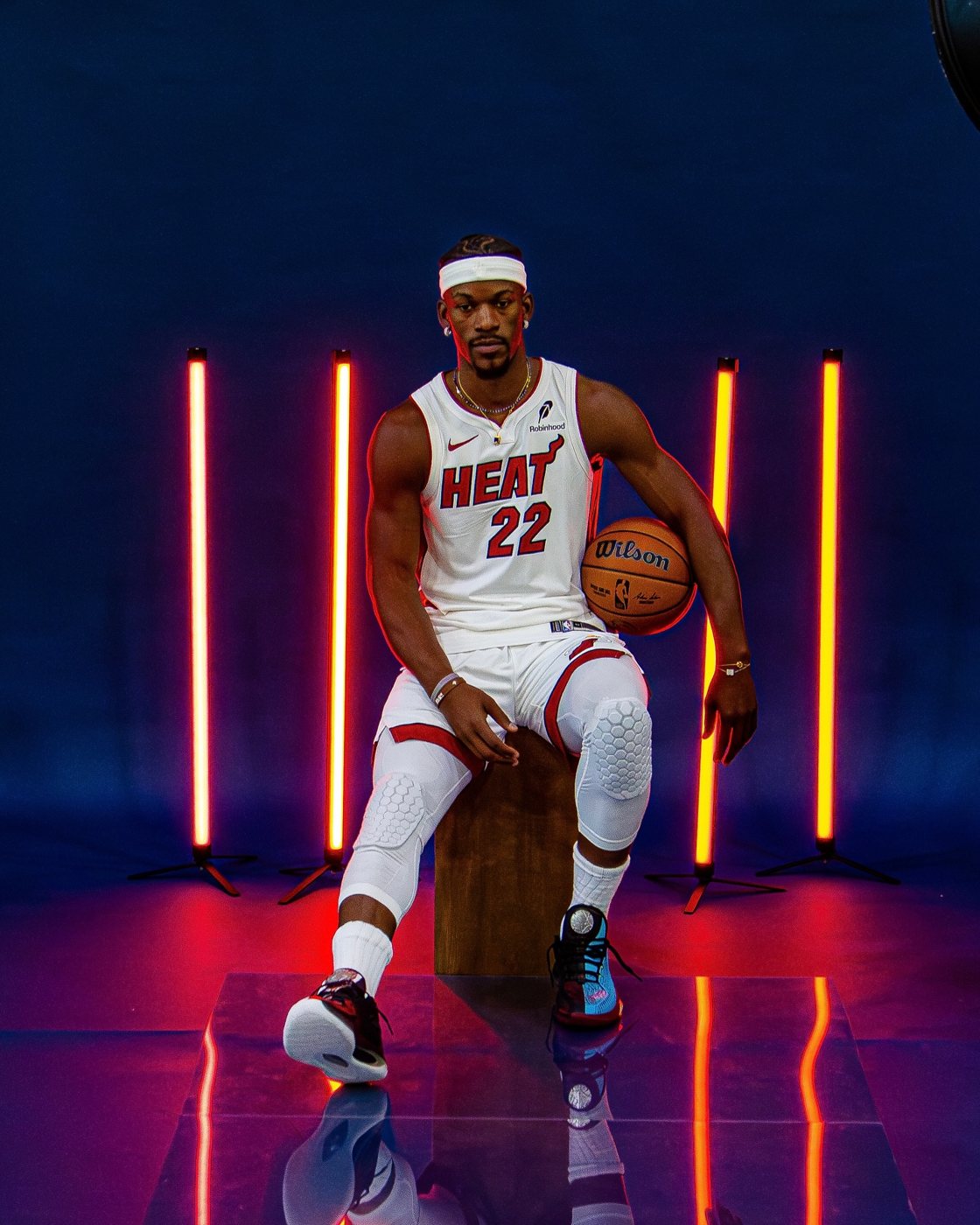 Jimmy Butler crouched with a basketball between orange neon light bars