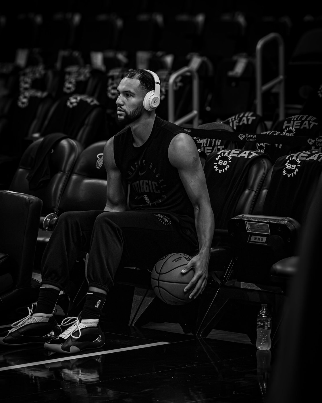 A Heat player in headphones sitting alone in the arena seats, in black and white