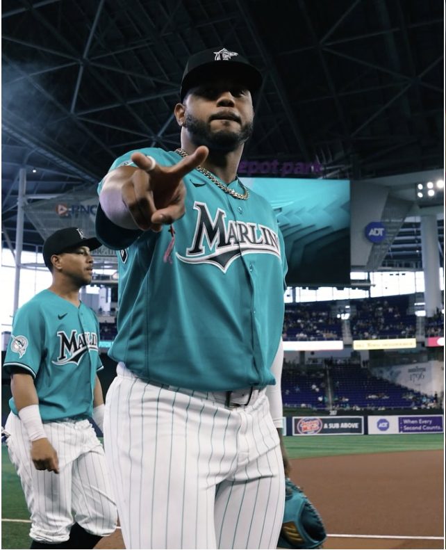 A Marlins player pointing at the camera in the teal throwback jersey