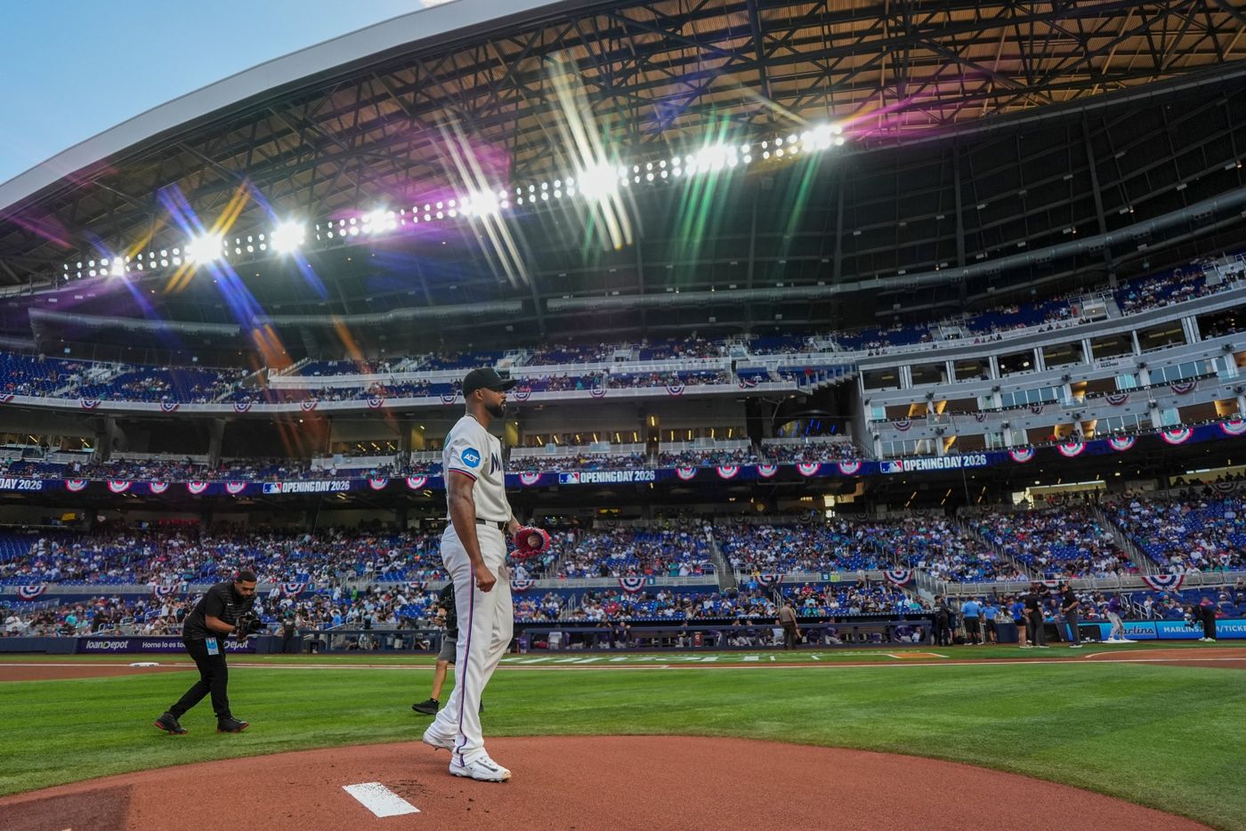 A Marlins pitcher on the mound under the lights with Opening Day 2026 banners